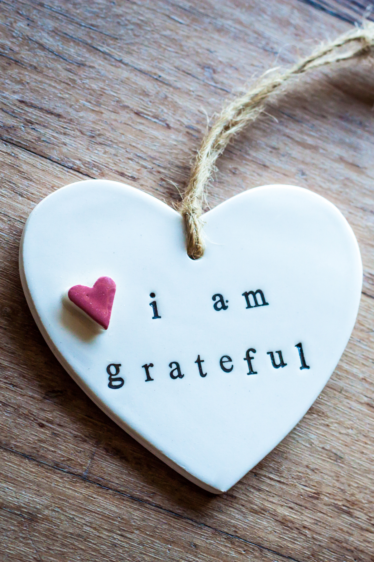 Heart-shaped ceramic plaque with 'i am grateful' text and a pink heart on a wooden surface