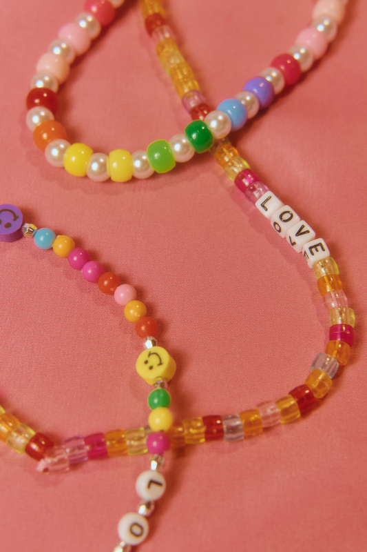 Colorful beaded necklaces with 'LOVE' and smiley face charms on a pink background